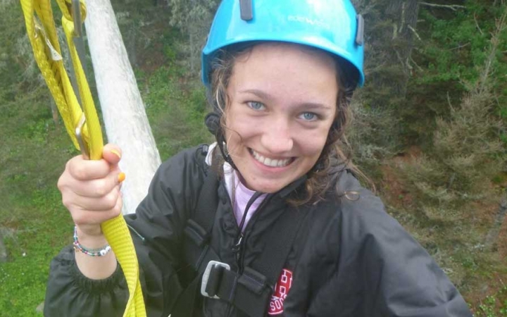 a student wearing a helmet smiles at the camera while participating in a high ropes course with outward bound
